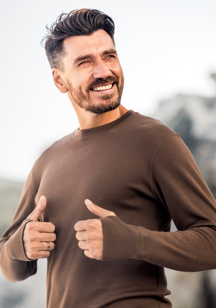 A man smiles and gives a thumbs up while wearing the Woolx Glacier Long Sleeve Crew in black, an odor-resistant shirt.
