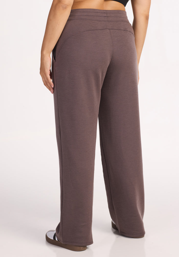 A person shown from the back against a plain light background wears Woolx Bree Lounge Pants in Plum Truffle, relaxed fit with straight legs, paired with black sandals.