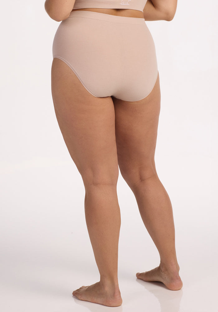 A person stands barefoot on a white background, shown from the back wearing Woolx's Mabel Full Coverage Underwear in Sand with a matching nude bra.