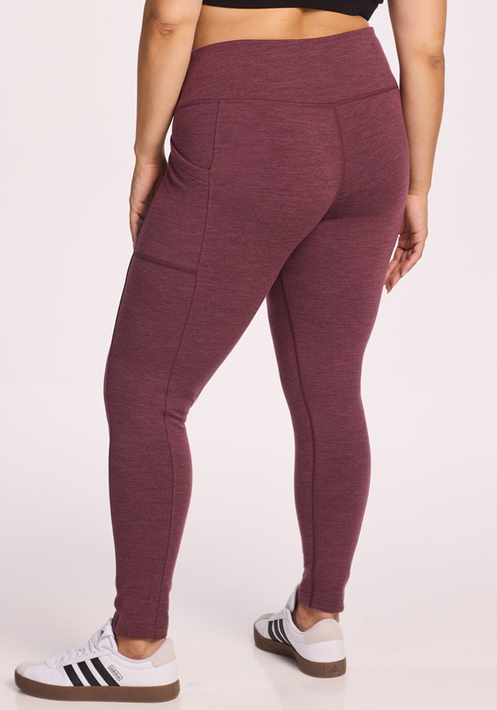 A person wearing Woolx Frost Duralite® Leggings in Grape Harvest Melange with side pockets and white Adidas sneakers, standing against a plain light background, shown from the back.