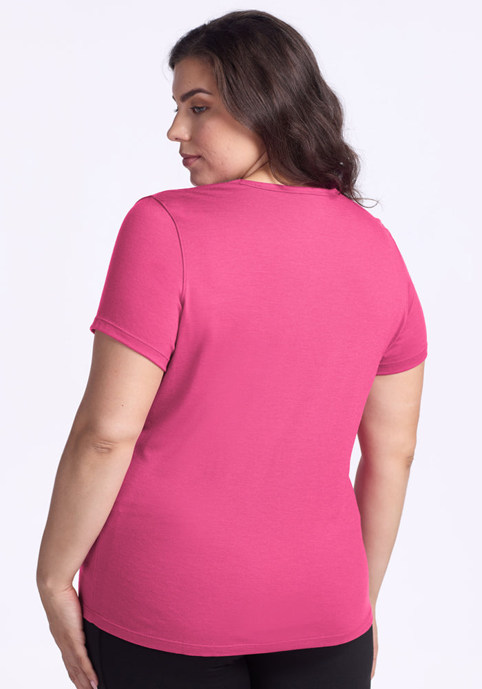 A woman with long dark hair stands facing away, wearing the Woolx Liza Crew Neck Tee in Raspberry Fizz and black pants against a plain white background.