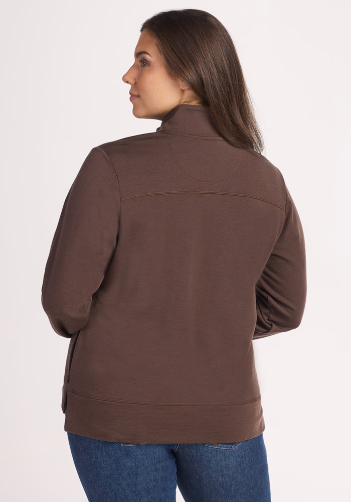 A woman with long brown hair is seen from behind, wearing the Woolx Annie 3 Button Pullover in Bracken and blue jeans, standing against a plain light-colored background.