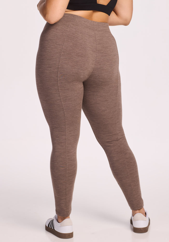 A person is shown from the back against a plain light background, wearing Woolx Stella Leggings in Simply Taupe, a black sports bra, and white sneakers with brown soles.