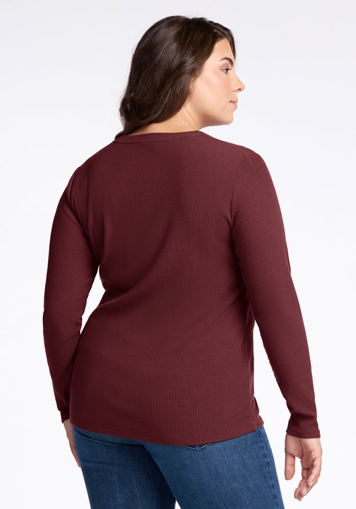 A woman with long brown hair faces away, wearing the Woolx Hadley Ribbed Crew in Toasted Garnet with blue jeans—ideal for lightweight layering or travel—set against a plain white background.