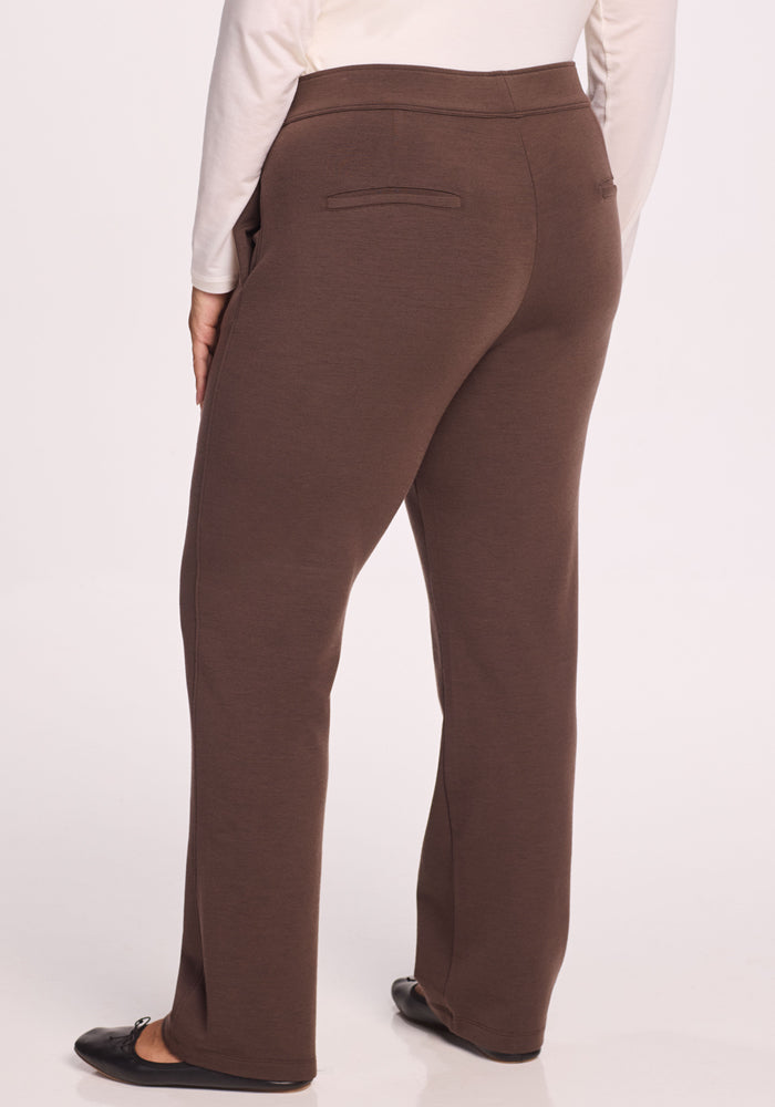 A person wearing Woolx Emerson Straight Leg Pants in Bracken, black shoes, and a white long-sleeve top is shown from the back.