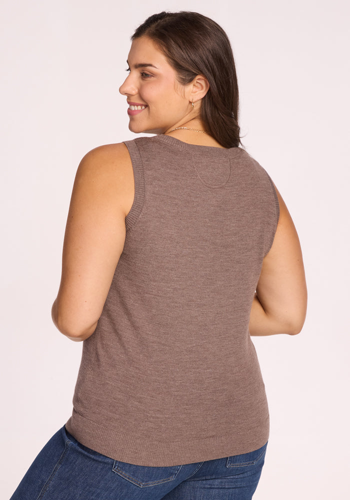 A woman with long brown hair smiles over her shoulder, wearing the Woolx Chessy Tank Top in Simply Taupe and blue jeans against a light background. This chic sleeveless sweater adds effortless style to her look.