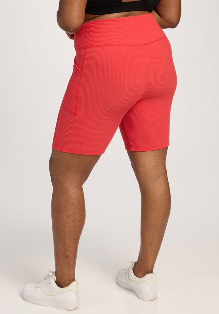 Model wears Woolx Miley Bike Shorts in Hibiscus with white sneakers, shown from the back against a plain background.