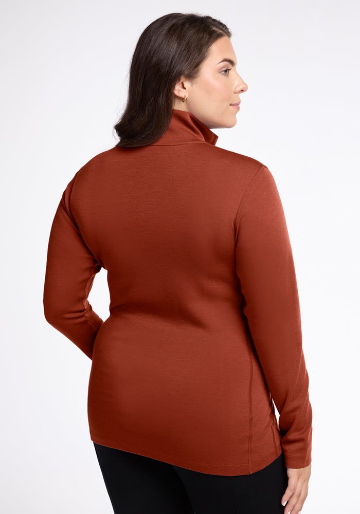 A woman faces away, wearing the Woolx Brooke 1/4 Zip in Maple Leaf and black pants against a plain white background.