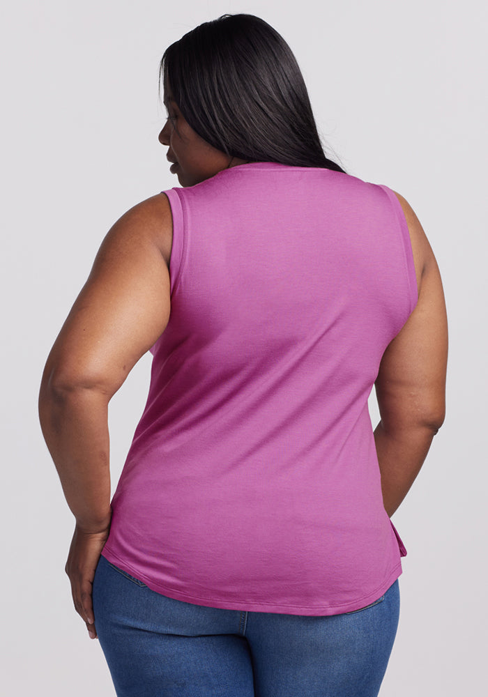A woman with long dark hair, wearing the Woolx Bella Tunic Top in Purple Wine and blue jeans, stands facing away from the camera against a plain light background.