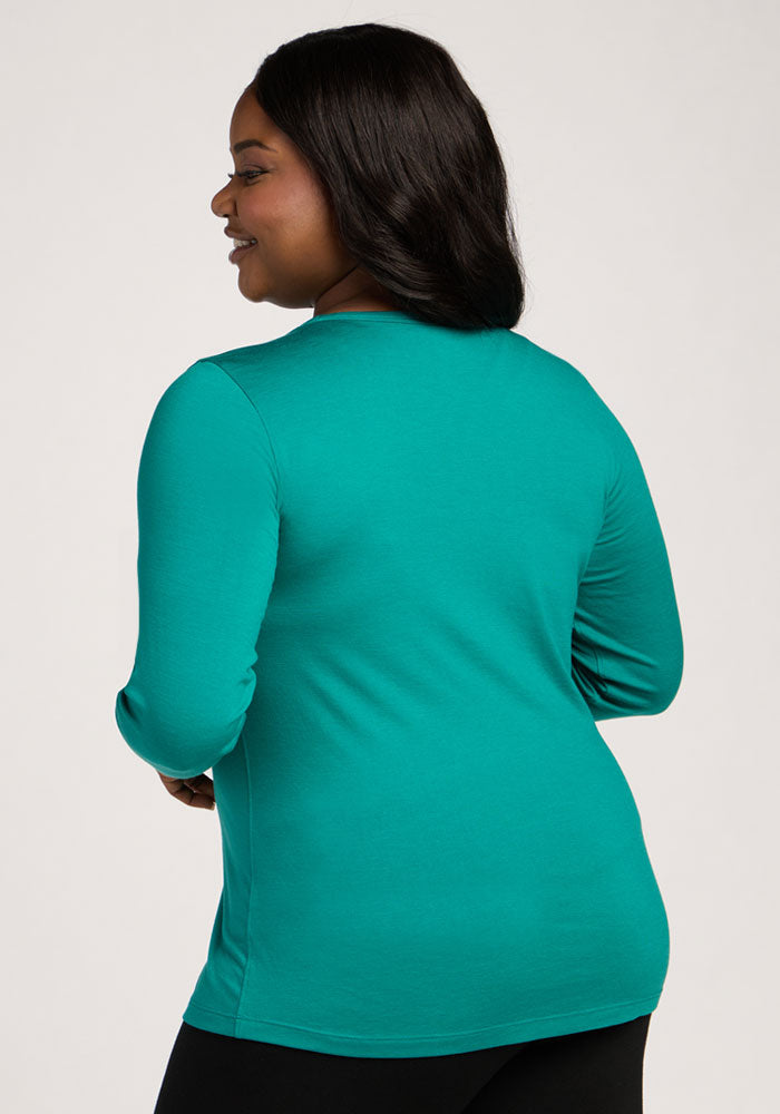 Woman with long dark hair wears a Woolx Remi Long Sleeve T-Shirt in Cabana Crush and black pants, smiling from the back.