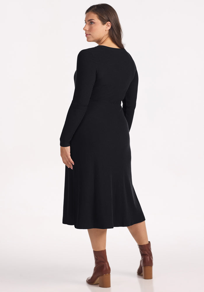 Woman in Woolx Caroline Ribbed Twirl Dress - Black, with brown ankle boots, standing with her back turned.