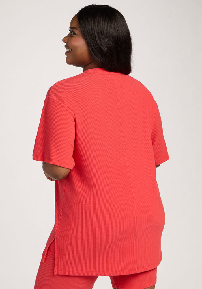 A woman with long dark hair wears the Woolx Vera Ribbed Tunic - Hibiscus with matching shorts.