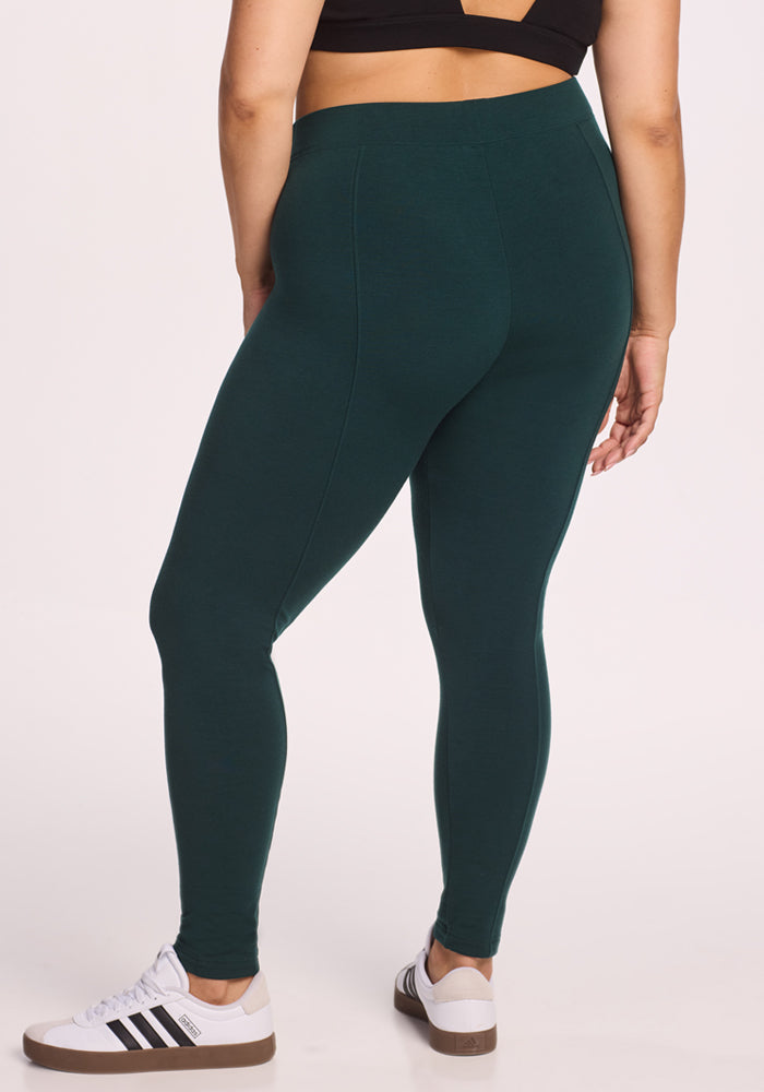 A person wearing Woolx Stella Leggings in Deep Timber and a black crop top, paired with white Adidas sneakers, stands with their back to the camera against a plain white background.