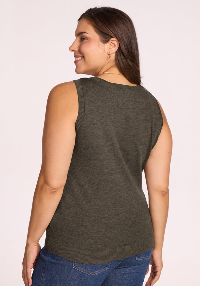 A woman with long brown hair is smiling and standing with her back to the camera, wearing the Woolx Chessy Tank Top in Pine Needle and blue jeans against a light, plain background.