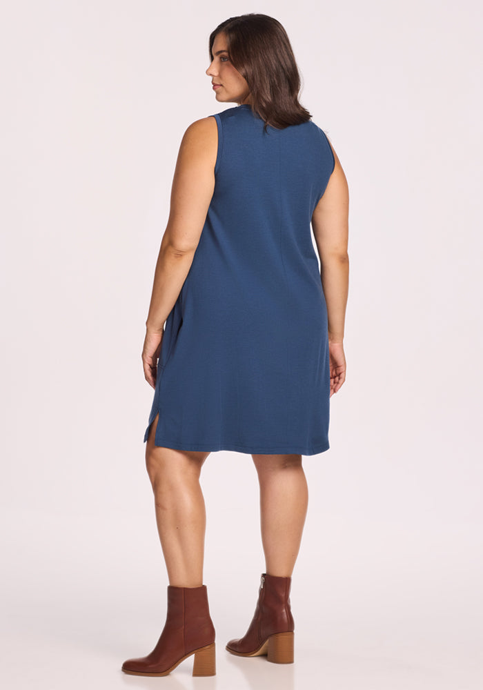 A woman with shoulder-length brown hair stands facing away in the Woolx Clara Dress - Starry Night, paired with brown block-heeled ankle boots. The background is plain white.