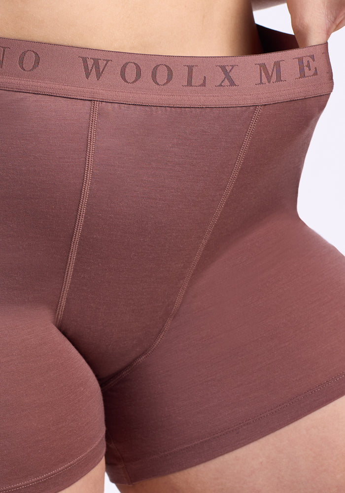 Close-up of a person wearing Woolx Elliott Boyshort in Nutmeg, pulling the waistband with their right hand; "WOOLX" is visible on the waistband. This underwear features temperature-regulating fabric.