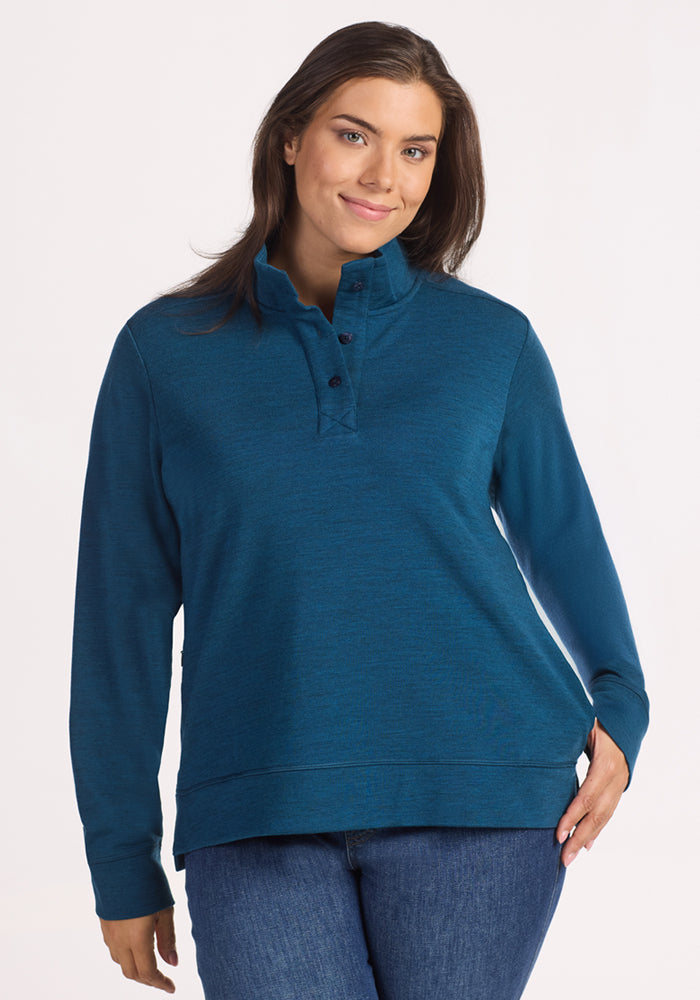 A woman smiles gently at the camera, wearing the Woolx Annie 3 Button Pullover in Majolica Blue with blue jeans, standing against a plain white background. 