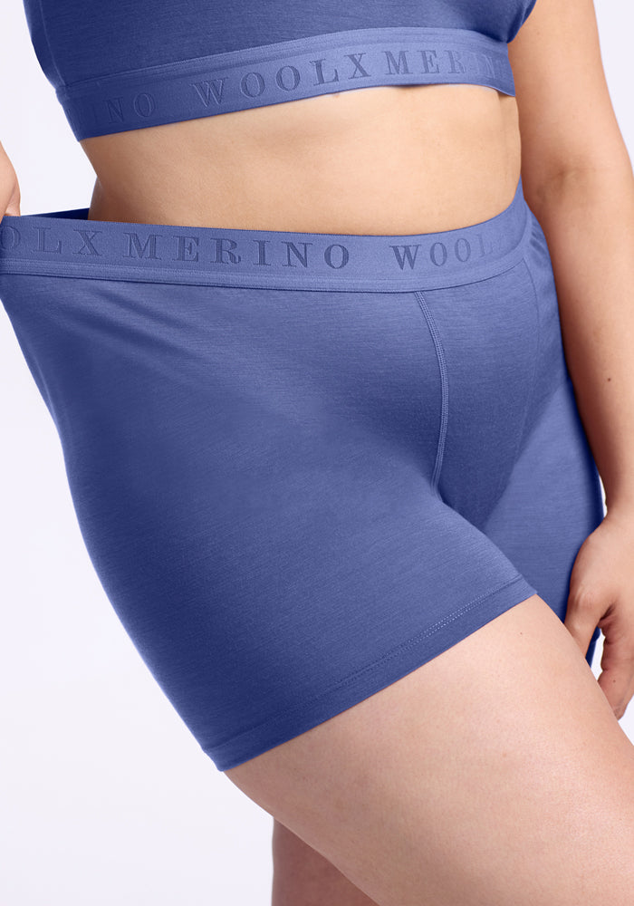 A person wearing Woolx Elliott Boyshorts in Cloudy Bay gently pulls the waistband, which reads "WOOLX MERINO", showing the comfortable, antimicrobial fit of these high-waisted Merino wool underwear.
