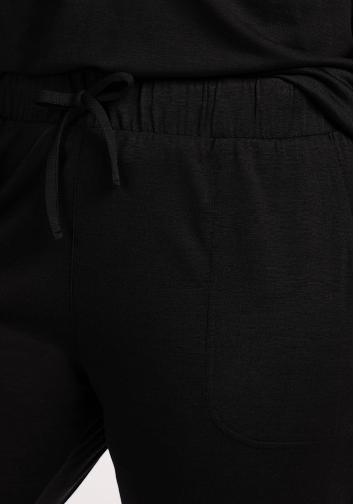 Close-up of a person wearing Woolx Mary Kate Lounge Pants in black, featuring a front pocket and matching top. The soft, moisture-wicking Merino wool fabric offers comfort—perfect for travel and lounging.