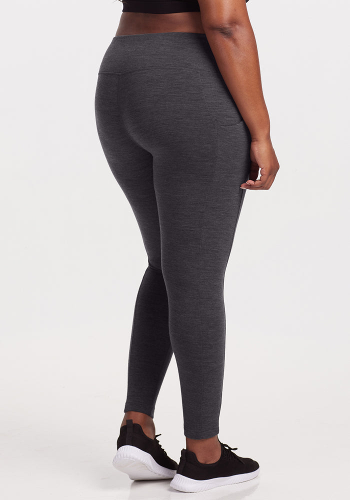 Someone wearing Woolx Piper Pocket Leggings in Cinder Melange, a black crop top, and black-and-white sneakers stands facing away from the camera against a plain white background.