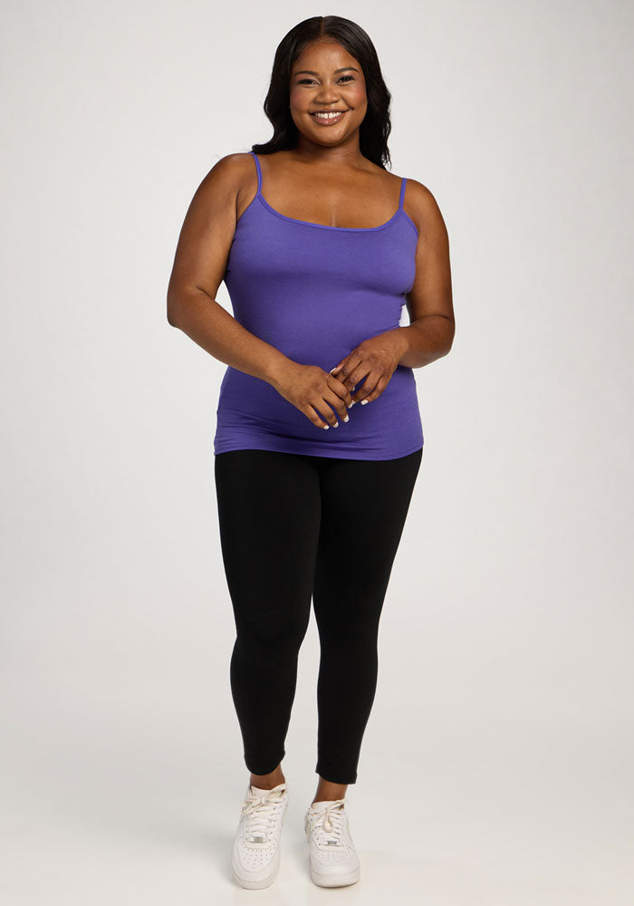A woman smiles in a Woolx Teagen Cami With Shelf Bra in Berry Indigo and black leggings against a plain background.