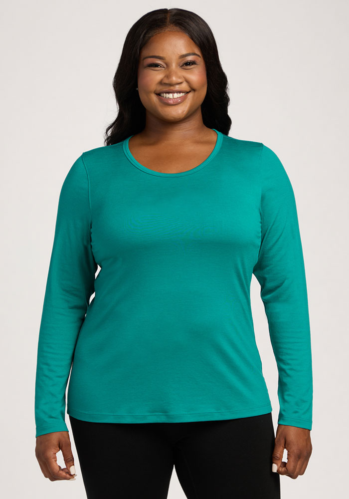 A woman smiles in a Woolx Remi Long Sleeve T-Shirt - Cabana Crush and black pants against a light background. 