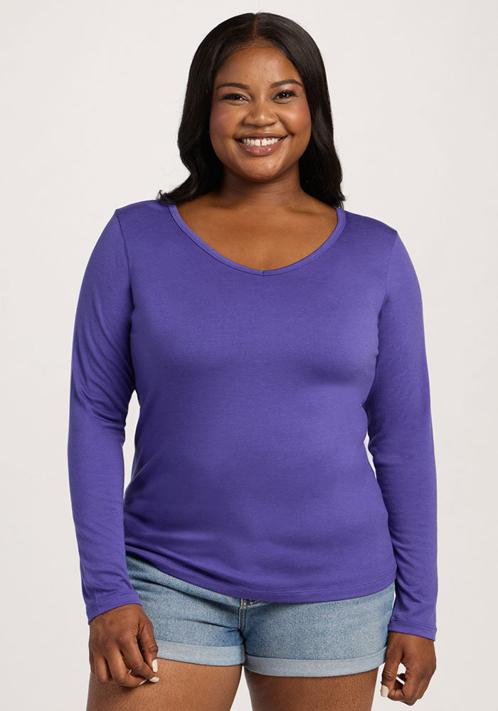 Smiling woman in a Woolx Layla V Neck Top - Berry Indigo and denim shorts stands against a light background. 