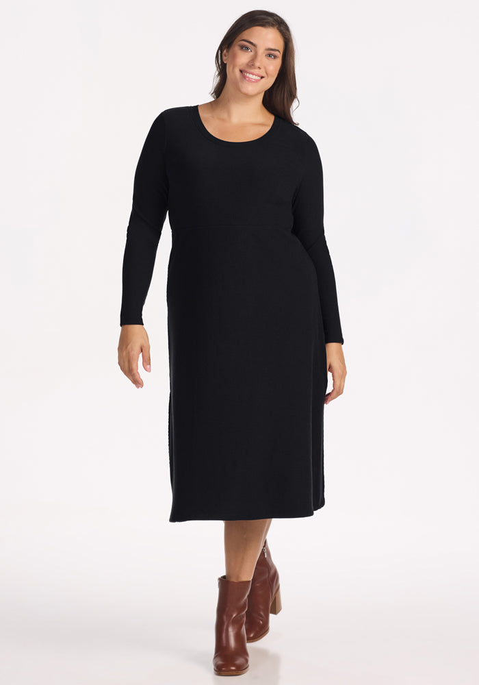 Woman in the Woolx Caroline Ribbed Twirl Dress - Black and brown ankle boots, smiling against a white background. 