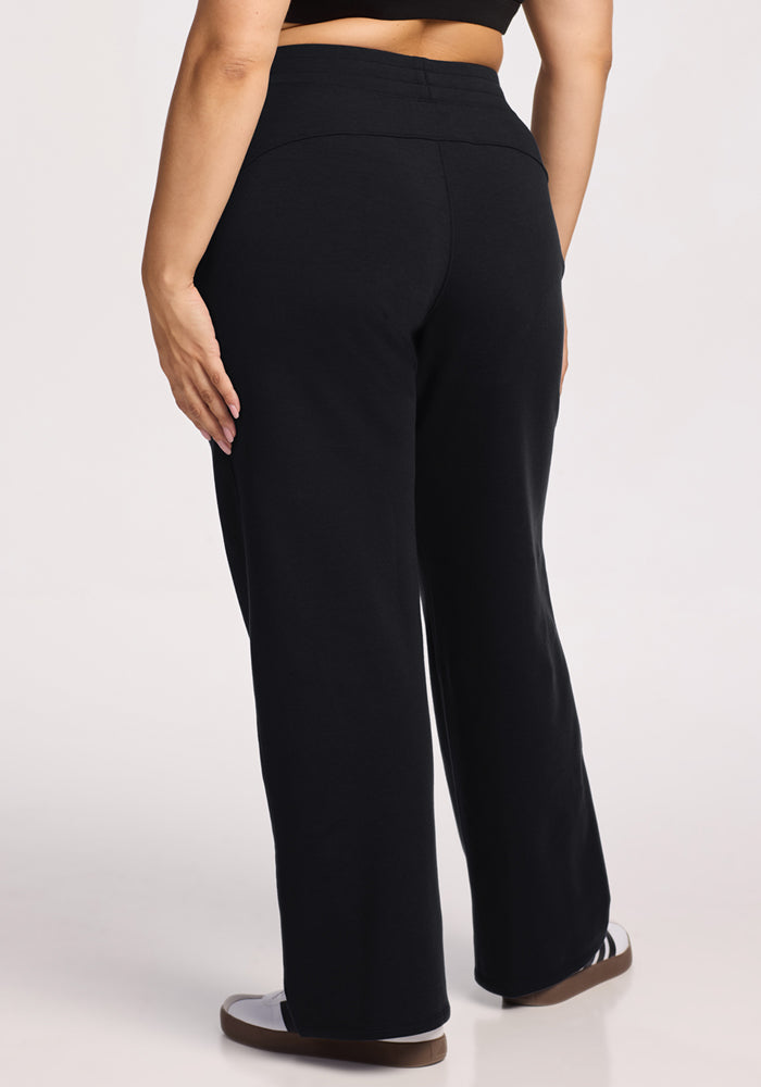 A person in Woolx Brynn Pants - Black, high-waisted and loose-fitting, is seen from the back wearing black-and-white sneakers against a light background.