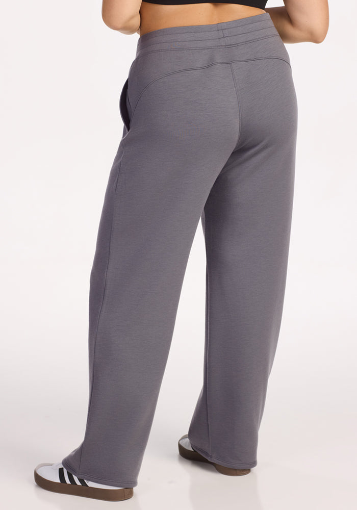 A person is shown from the back, standing against a plain white background, wearing Woolx Bree Lounge Pants in Arctic Dusk and black-and-white slip-on shoes.