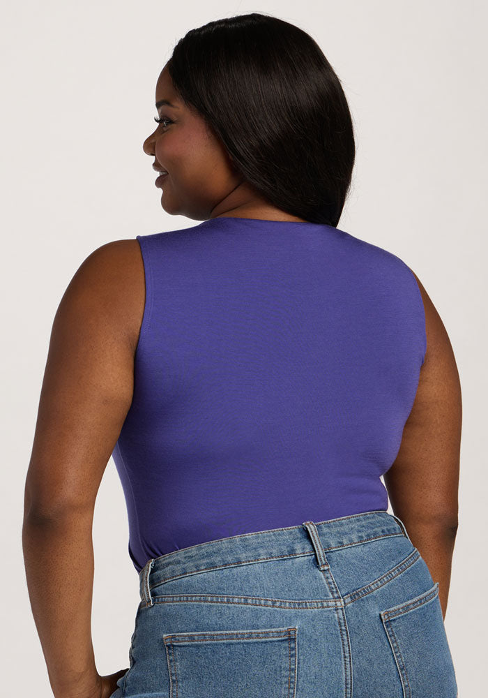 A woman wears the Woolx Maggie Bodysuit in Berry Indigo with high-waisted blue jeans, her long dark hair flowing.