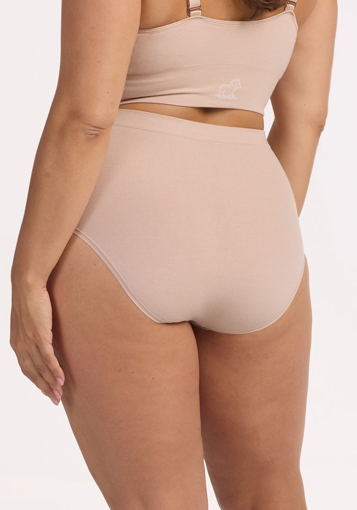A person wears Woolx Mabel Full Coverage Underwear in Sand, shown from the back against a plain light background, highlighting the seamless comfort and fit of this high-waisted underwear.