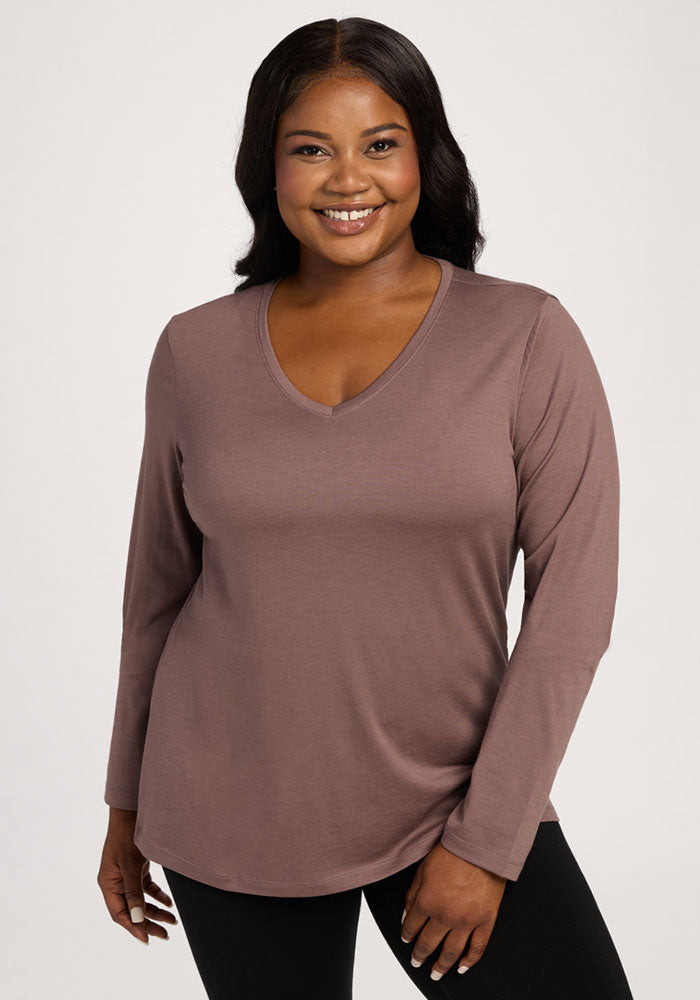 Smiling woman wears the Woolx Millie Long Sleeve in Peppercorn with black pants against a plain light background. 