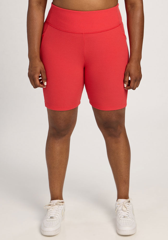 Person wearing Woolx Miley Bike Shorts in Hibiscus and white sneakers, standing against a plain light background. 
