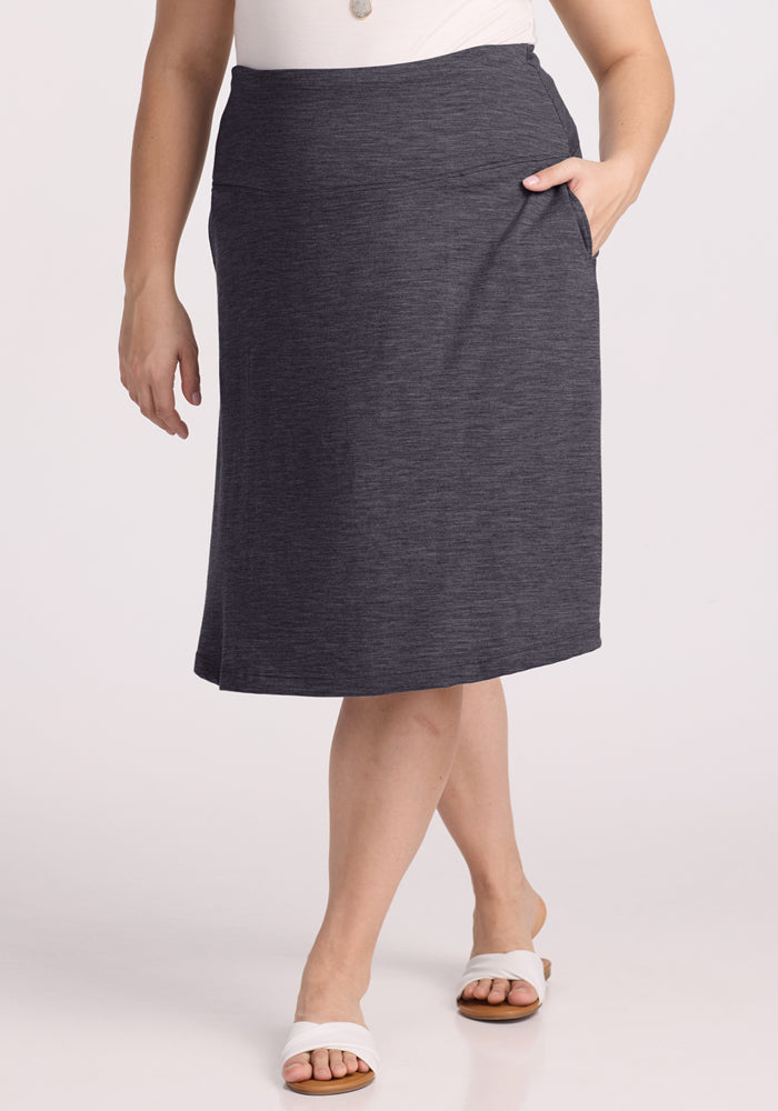 A person wearing the Woolx Marilyn Flowy Midi Skirt in Cinder Melange, paired with a white top and white slide sandals, stands against a plain light background.