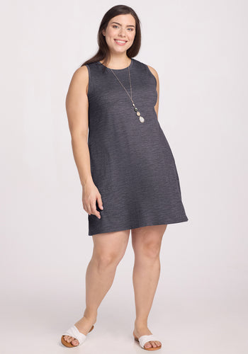 A woman smiles against a plain light background wearing the Woolx Clara Dress in Cinder Melange, paired with white sandals and a long necklace. | Juliana is 5'10", wearing a size XL