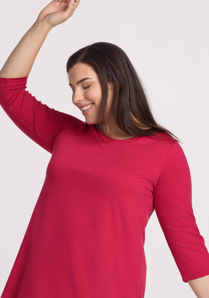 A woman with long dark hair smiles with her eyes closed and raises one arm, wearing the Woolx Rissa A Line Dress in Poppy Spark against a plain white background.