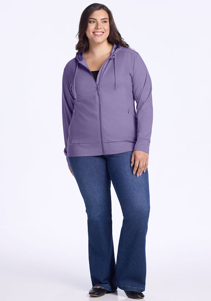 A woman smiles against a white background, wearing the Woolx Ryann Hoodie in Montana Grape, paired with dark blue bootcut jeans and black shoes.