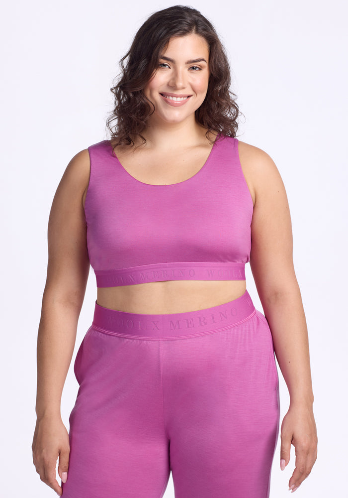 A woman with wavy brown hair smiles while wearing the Woolx Aubrey Lounge Bra in Wild Blossom, standing against a plain white background.