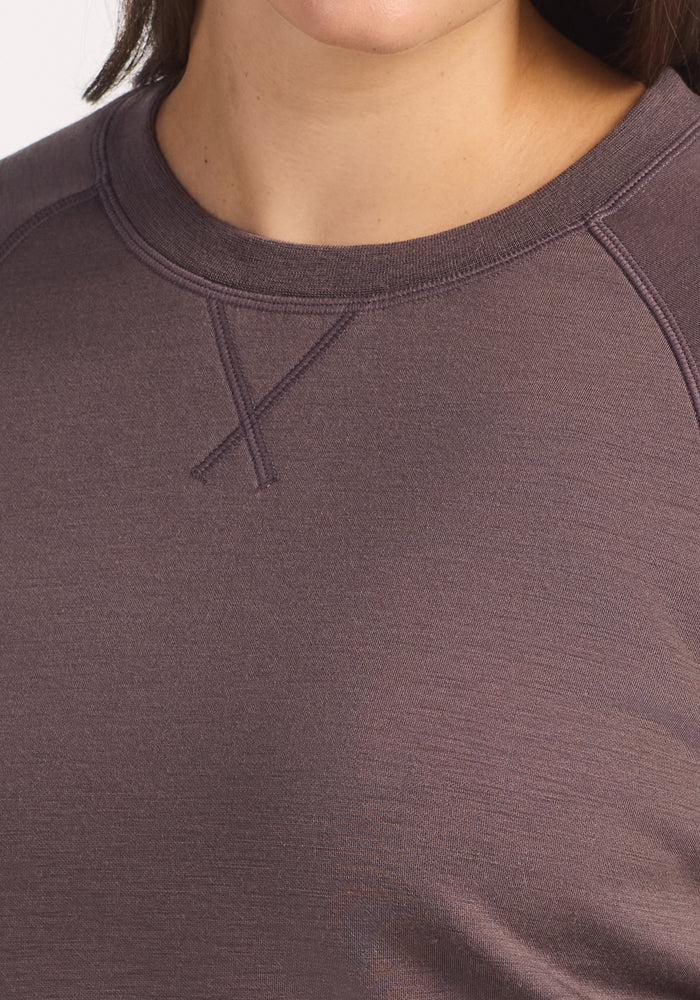 Close-up of a person wearing the Woolx Bailey Crewneck Sweatshirt in Plum Truffle, made from recycled polyester, with visible stitching near the collar and the lower face and neck partially shown.