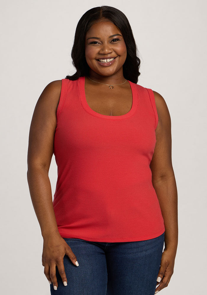 Smiling woman wears the Woolx Sloane Ribbed Tank in Hibiscus and jeans, standing against a light background. 
