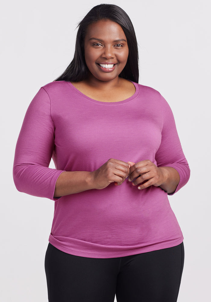 A woman with long dark hair smiles at the camera, wearing the Woolx Jenny 3/4 Sleeve Crew Neck in Purple Wine and black pants, posing against a plain light background. 