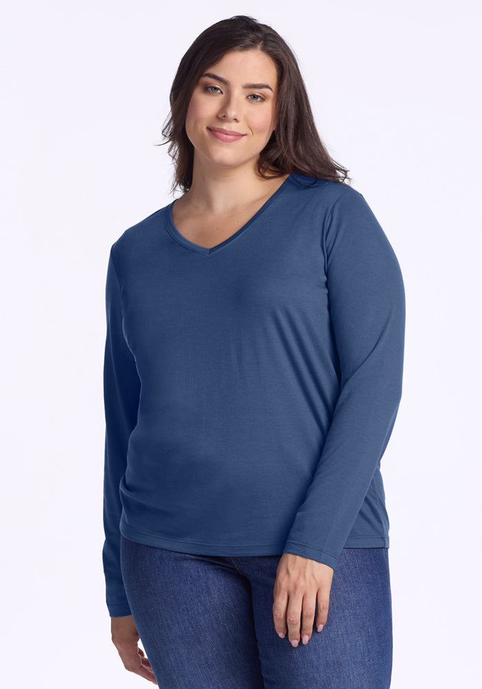 A woman with long brown hair is wearing the Woolx Millie Long Sleeve - Starry Night and blue jeans, standing against a plain white background and smiling softly. 