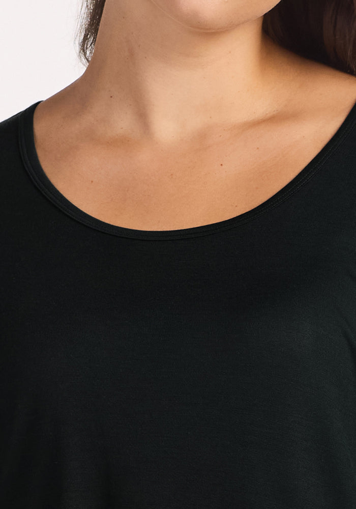 A close-up of a person wearing the Woolx Lucille Long Sleeve Nightgown in black highlights their neck and collarbone, drawing attention to the eco-friendly merino wool’s soft, elegant texture against a plain background.