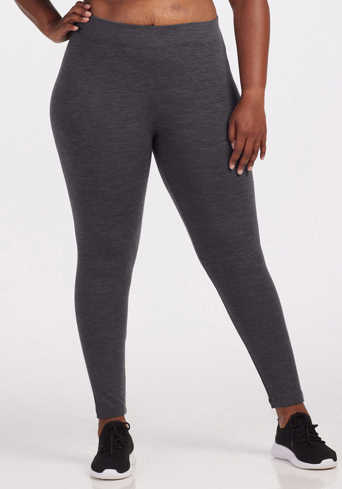 A person wearing Woolx Stella Leggings in Cinder Melange and black sneakers stands against a plain white background, with one hand on their hip. 