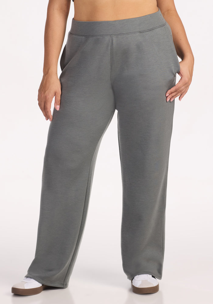 A person wears Woolx Bree Lounge Pants in Sedona Sage, featuring ultra-soft fleece and a high-waisted fit, hands in pockets, paired with white sneakers; shown from the waist down against a plain light background.