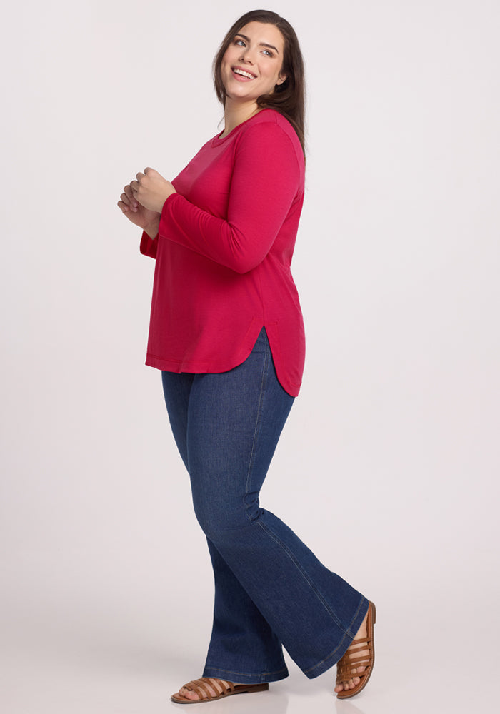 A woman wearing the Woolx Hazel Tunic in Poppy Spark smiles and looks upward, enjoying the comfort of its temperature-regulating merino wool against a plain light background.