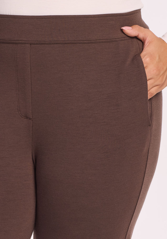 A close-up shows a person wearing Woolx Emerson Straight Leg Pants in Bracken, featuring a sleek, high-waisted fit, wide waistband, and one hand in the pocket for a smooth, tailored look.