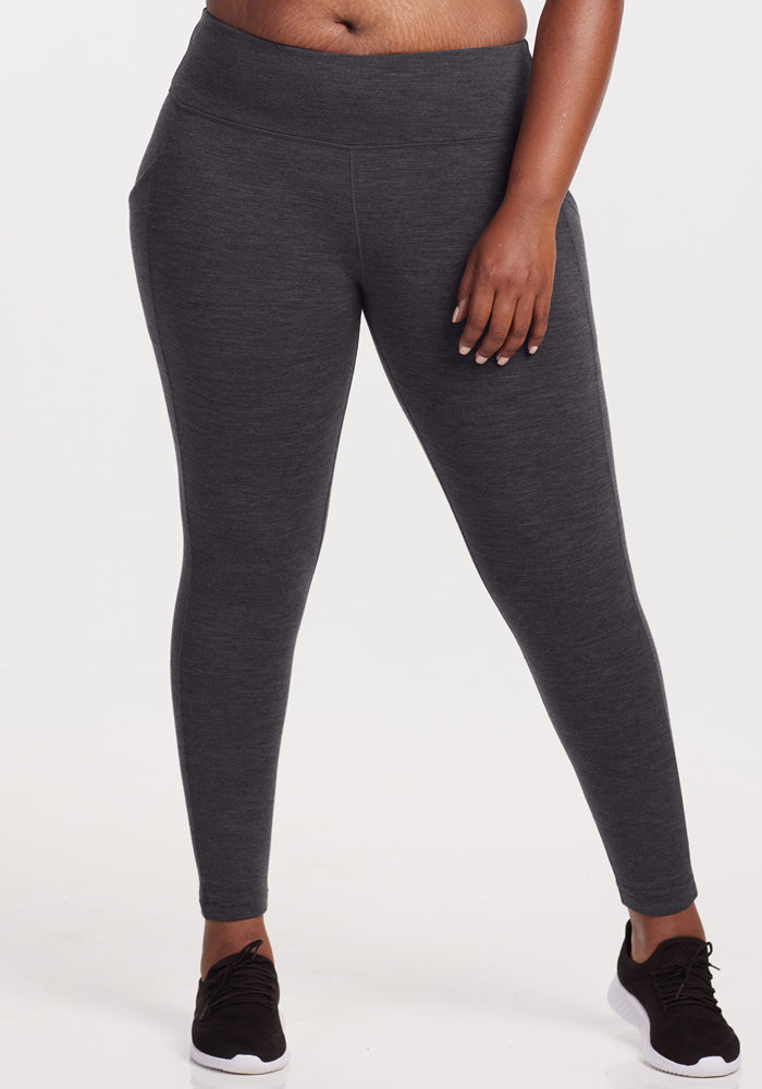 A person wears Woolx Piper Pocket Leggings in Cinder Melange with black sneakers, standing against a white background. The image is cropped from the chest down to highlight the fit of these women's Merino wool baselayer leggings. 