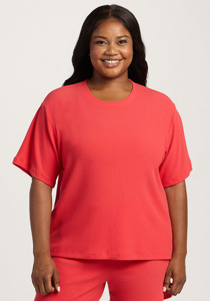 Smiling woman wears Woolx Delia Ribbed Short Sleeve in Hibiscus, paired with matching pants, against a plain background. 